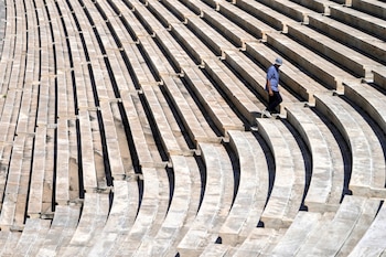 Gradas de piedra de un estadio con numerosas filas y pasillos. Un hombre con camisa azul, pantalón oscuro y sombrero claro desciende por las escaleras
