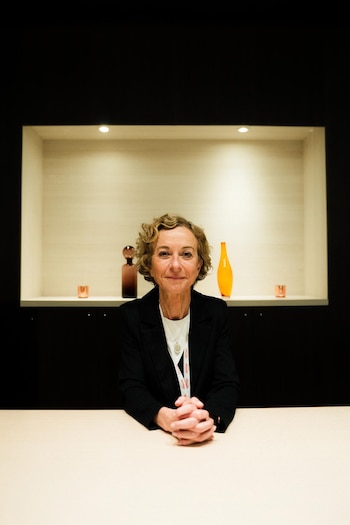 Noemí Reguart sentada frente a una mesa clara, mirando a cámara con las manos entrelazadas; detrás hay un nicho iluminado con objetos decorativos