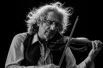 Un hombre con anteojos, camisa y chaleco toca un violín en una imagen en blanco y negro.