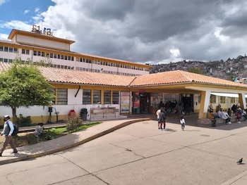 Vista exterior del edificio del Hospital Regional del Cusco con personas cerca de la entrada y cerros al fondo bajo un cielo nublado