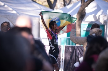 Un corredor de atletismo sostiene la bandera de Etiopía sobre su cabeza frente a espectadores y carpas blancas