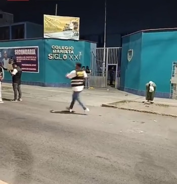 Vista nocturna exterior del Colegio Marista Siglo XXI con una vereda y calle en primer plano. Varias personas se ven cerca de la entrada del edificio