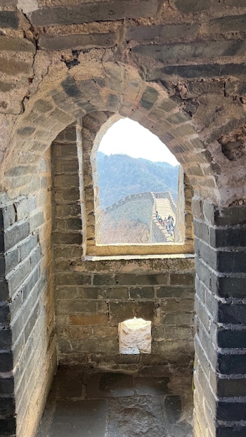 Vista desde el interior de una torre de la Muralla China a través de un arco, mostrando la muralla con turistas y montañas al fondo bajo un cielo claro