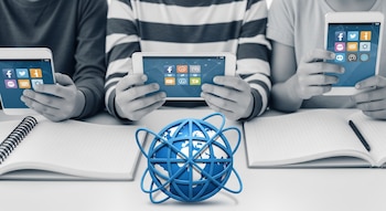 Tres pares de manos infantiles sostienen dos teléfonos móviles y una tableta con pantallas de aplicaciones. Un globo azul que representa internet está en primer plano, flanqueado por cuadernos.