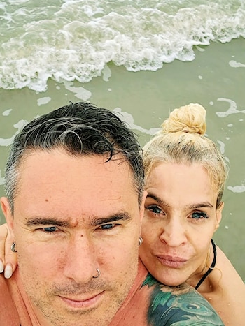 Selfie de Leticia Brédice con cabello rubio recogido y un hombre con cabello oscuro y tatuajes, en el mar con olas