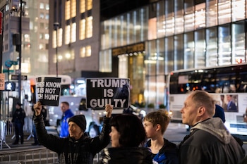 Un manifestante sostiene pancartas contra el expresidente Donald Trump frente a la Torre Trump en Nueva York la noche del lunes 3 de abril de 2023. (AP Foto/Corey Sipkin)