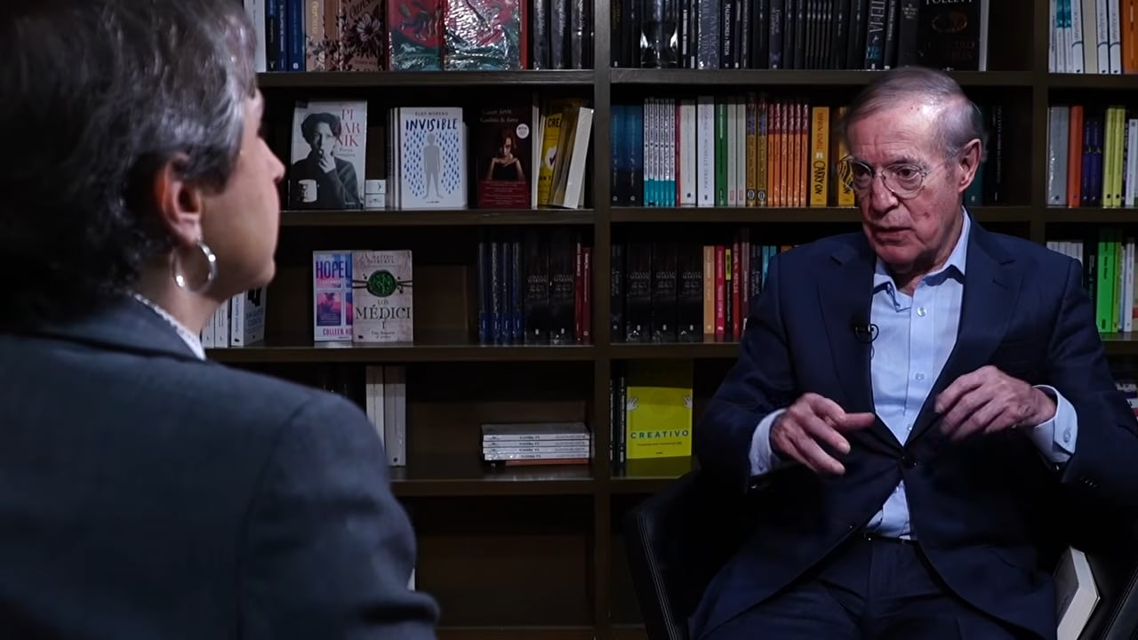 José Ramón Fernández es entrevistado por Carmen Aristegui, ambos sentados frente a una estantería llena de libros. (Carmen Aristegui: YouTube)