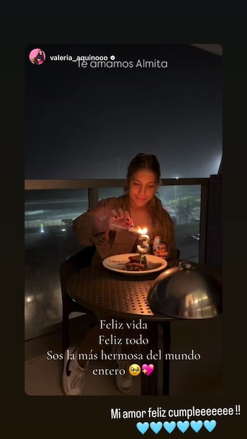 Joven mujer enciende una vela con el número tres en un pastel. Mesa redonda, copa metálica y fondo oscuro con luces de ciudad