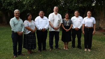 Seis personas, tres hombres y tres mujeres, posan de pie sobre pasto. Al fondo, vegetación. Un hombre lleva un parche de bandera de Guatemala en su camisa