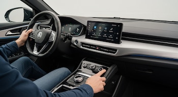 Interior de un automóvil eléctrico moderno con tablero, controles físicos y conductor interactuando.