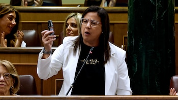 Una mujer con gafas y chaqueta blanca sostiene un pequeño espray negro frente a un micrófono en un parlamento