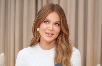 Primer plano de Khloe Kardashian, una mujer con cabello castaño ondulado y ojos verdes claros, usando un top blanco y aretes dorados, mirando hacia la izquierda