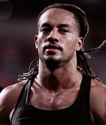Primer plano de André Carrillo, un hombre con dreadlocks y bigote, vistiendo una camiseta de tirantes negra y piel sudorosa