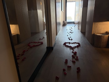 Pétalos de rosa rojos repartidos por un pasillo con suelo de madera formando un corazón, junto a un espejo que los refleja