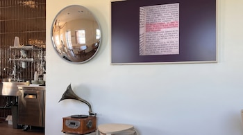 Interior: espejo convexo, pantalla con texto bíblico resaltado, gramófono vintage, encimera de acero inoxidable y pared de baldosas marrones.