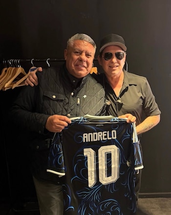 Andrés Calamaro, con gorra y gafas, posa junto a Claudio Tapia. Ambos sostienen una camiseta de fútbol negra con el nombre 'Andrelo' y el número 10
