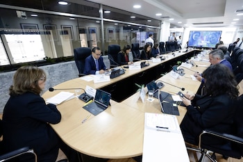 Diversas autoridades permanecen sentadas alrededor de una gran mesa de reuniones redonda con micrófonos, computadoras y letreros con sus nombres