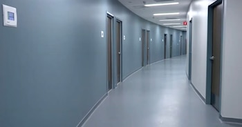 Un pasillo interior curvo con paredes azul grisáceo y un suelo gris claro. Hay puertas idénticas a lo largo de las paredes y luces de techo rectangulares