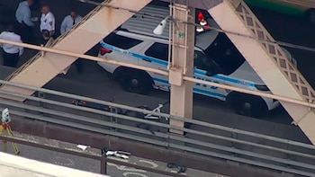 Vista aérea de un vehículo policial con luces encendidas y varios agentes en un puente. Un patín eléctrico yace en el suelo