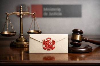 Balanza de justicia dorada, mazo de madera, sobre crema con escudo del Perú en relieve rojo sobre mesa de madera. Fondo borroso con logo Ministerio de Justicia.