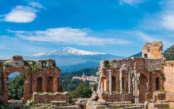 Ruinas de ladrillo con arcos y columnas en primer plano, con un volcán cubierto de nieve y cielo despejado al fondo
