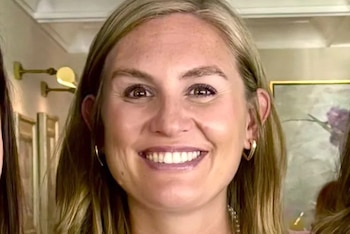 Primer plano de mujer con cabello rubio, ojos marrones, sonrisa, dientes visibles, aretes dorados. Se observa parte de otra persona en el lado izquierdo