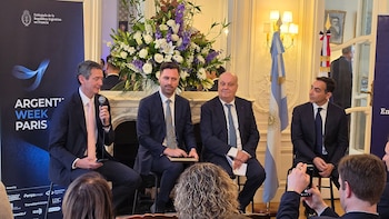 Cuatro hombres en traje sentados en un panel junto a la bandera de Argentina y un cartel del evento Argentina Week Paris