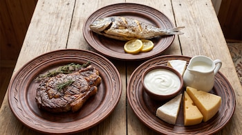 Tres platos de cerámica sobre una mesa de madera. Pescado asado con limón, corte de carne con hierbas, y otro plato con queso, leche y yogur.
