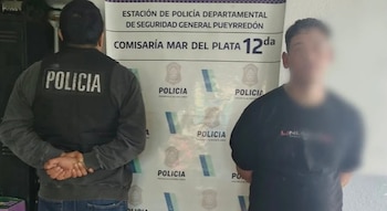 Un agente de policía de espaldas y un joven detenido con el rostro borroso permanecen de pie ante un cartel oficial
