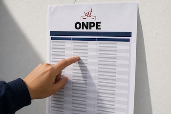 Una mano apunta a un listado impreso pegado en una pared blanca con el logotipo de la ONPE en la parte superior.