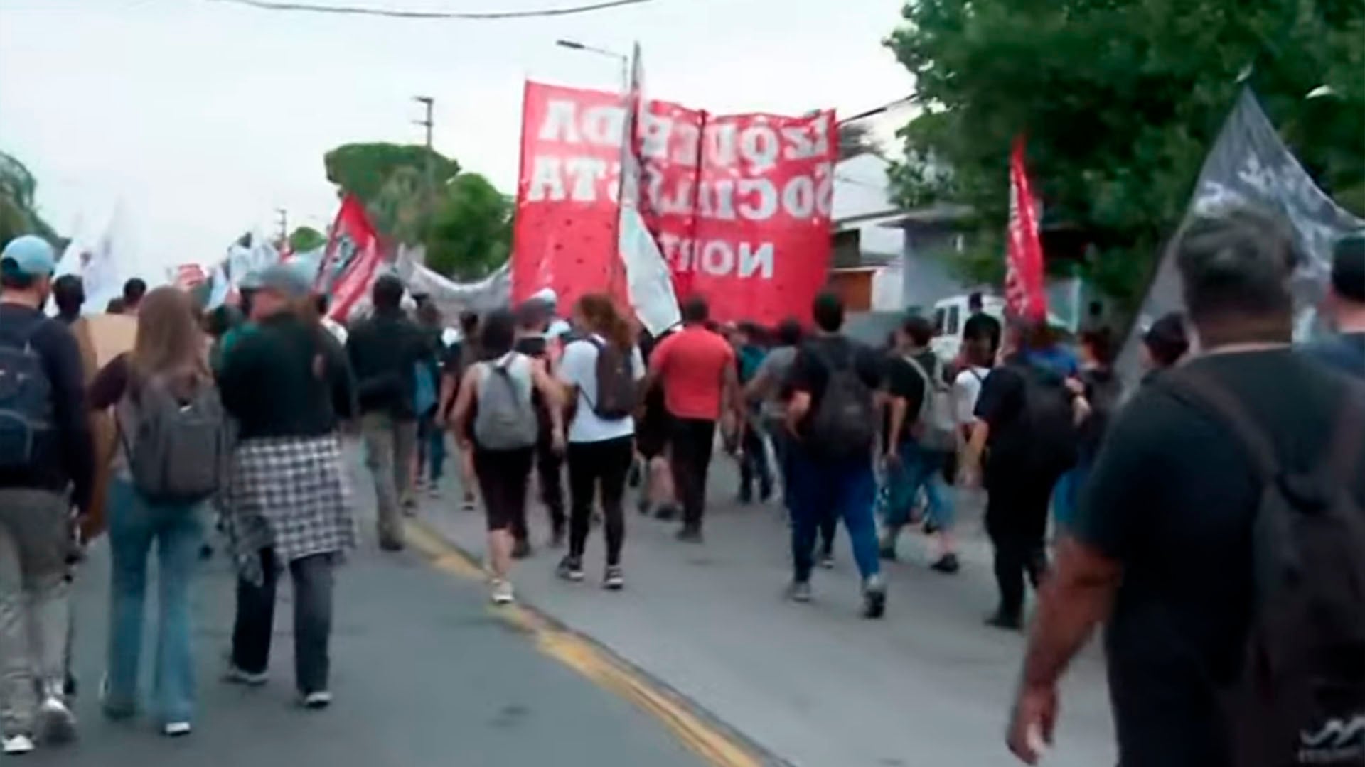 Un grupo numeroso de trabajadores de FATE marcha por una calle llevando pancartas rojas y blancas, dirigiéndose hacia la Panamericana para protestar por sus derechos. (Captura de video)