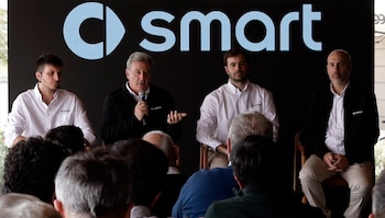 Cuatro hombres sentados frente a un panel negro con el logotipo de smart mientras uno habla por micrófono ante el público