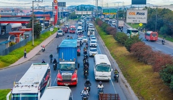 Carretera asfaltada con flechas pintadas en el suelo, un letrero verde con indicaciones hacia Bogotá y Funza, vehículos y árboles