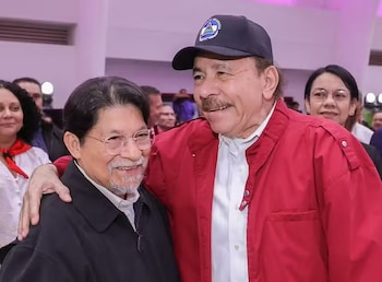 Daniel Ortega, con gorra azul y chaqueta roja, sonríe y abraza a Denis Rolando Moncada Colindres, quien lleva gafas y barba, en un evento público