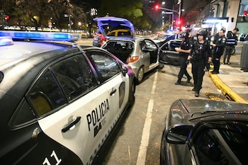 Un patrullero de la Policía de la Ciudad junto a un automóvil gris inspeccionado por agentes uniformados de noche en una avenida urbana