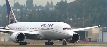 Un avión comercial blanco de la aerolínea United sobre una pista de rodaje, con árboles y hangares en el fondo