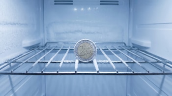 Una moneda de 2 Euros cubierta de hielo y escarcha en el centro de una rejilla metálica dentro de un congelador muy frío y con capas de hielo.