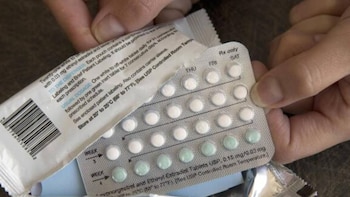 Una mano sostiene un blíster de píldoras anticonceptivas con pastillas blancas y verdes, junto a parte de su empaque con texto descriptivo