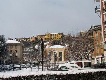 Paisaje urbano invernal de Piazzo Biella con edificios de colores, tejados cubiertos de nieve, coches aparcados y árboles sin hojas