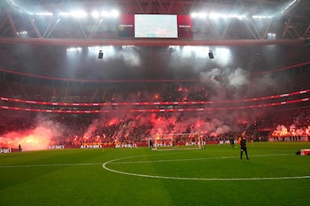 Campo de fútbol verde en el estadio del Galatasaray, iluminado por el resplandor rojo y el humo de las bengalas encendidas por los aficionados en las gradas