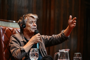 Emmanuel Carrère con auriculares y un micrófono en la mano gesticula mientras permanece sentado