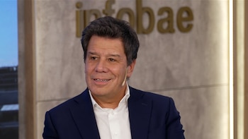 Primer plano de Facundo Manes sonriendo, vistiendo un traje azul oscuro y camisa blanca, con un micrófono de solapa. Detrás, el logo de Infobae es visible
