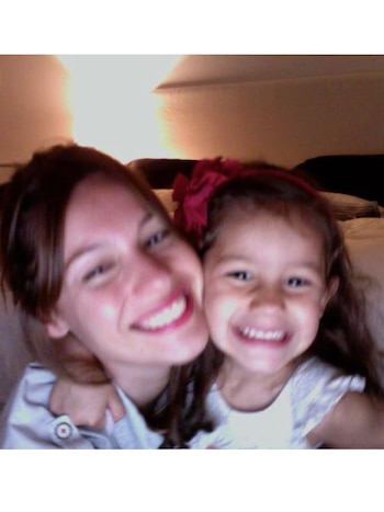 Una mujer sonriente con cabello castaño abraza a una niña también sonriente con cabello castaño y un lazo rosa en la cabeza