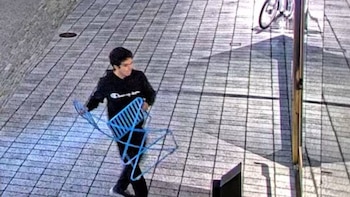 Una imagen de vigilancia muestra a un hombre con una sudadera oscura, identificado como Sam Altman, caminando y llevando una silla de metal azul