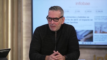 Hombre de cabello gris y gafas, con suéter oscuro, sentado. Tiene un micrófono de solapa. Detrás, una pantalla muestra texto y el logo Infobae