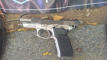 Primer plano de una pistola semiautomática Bersa Thunder de dos tonos (plateado y negro) sobre pavimento, con una vaina de bala sobre el cañón