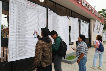 Personas consultan carteles con mesas de sufragio en la entrada de la Universidad Nacional Mayor de San Marcos (UNMSM), visible un edificio de ladrillo rojo y una reja