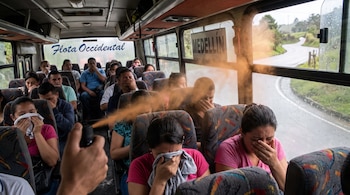 Un grupo de personas dentro de un bus cubre sus caras; una nube de gas pimienta se expande desde una mano que sostiene un rociador.
