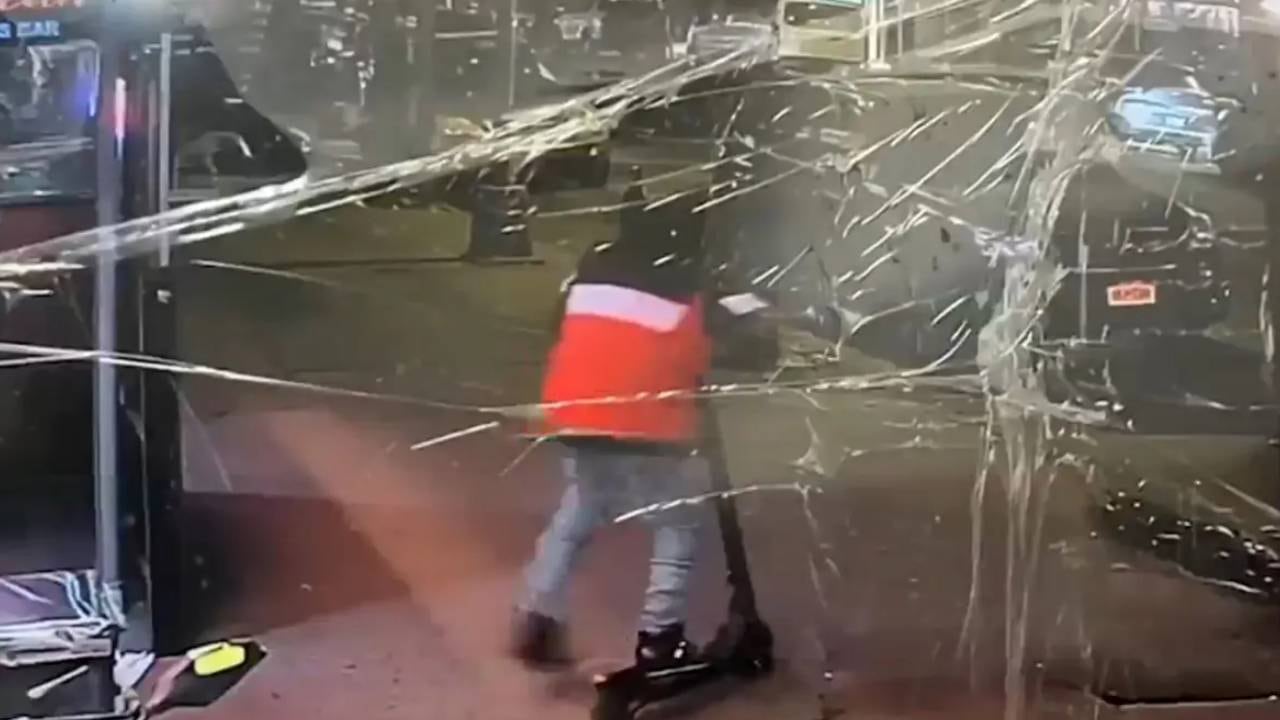 Un individuo en patineta eléctrica es captado a través de un cristal dañado en el incidente ocurrido en Queens. (NBC Nueva York)