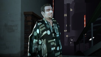 Hombre con camisa de patrón geométrico oscuro y claro, barba y pelo oscuro, de pie en un entorno urbano nocturno con edificios en segundo plano